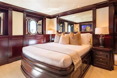 A luxurious bedroom with a large bed in the foreground and ornate wooden paneling and mirrors in the background.