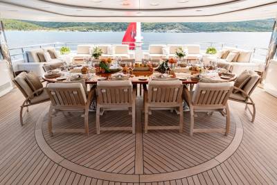 A beautifully set dining table on a yacht's deck faces a serene ocean and lush green hills.