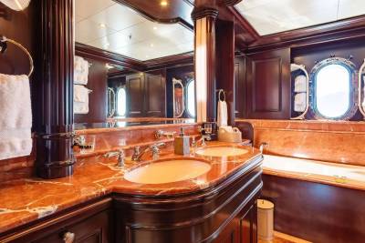 A luxurious bathroom with a marble countertop and double sinks in the foreground, and a bathtub and oval windows in the background.