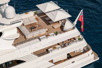 A luxurious white yacht with ample deck seating and umbrellas floats on the blue ocean.