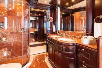 A luxurious bathroom with a marble shower in the foreground and a double vanity with mirrors reflecting the opulent interior in the background.