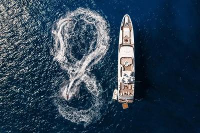 A jet ski creates a figure-eight wake in the deep blue ocean beside a large white yacht.