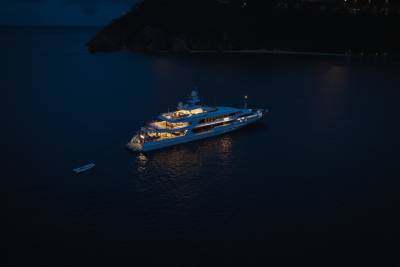 A large, illuminated yacht floats on dark water in the foreground, with a distant, dimly lit coastline in the background.