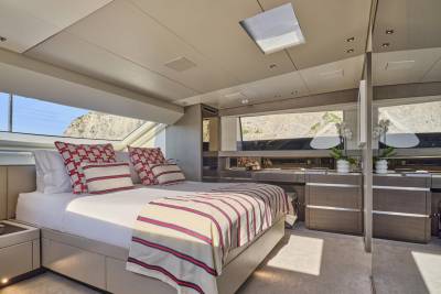 A luxurious yacht bedroom with a king-sized bed in the foreground and a scenic view of rocky cliffs through the windows in the background.