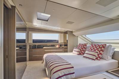A luxurious yacht bedroom with a neatly made bed in the foreground and large windows offering a view of the sea in the background.