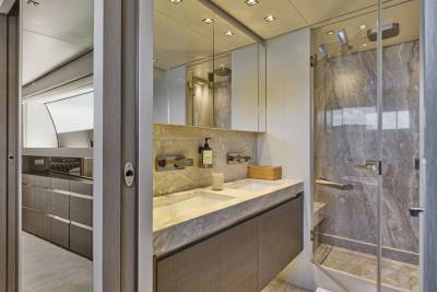 A modern bathroom with a double vanity and marble shower is visible in the foreground, while a glimpse of a galley kitchen can be seen through an open doorway in the background.