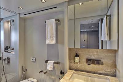 A modern bathroom with a sink and marble countertop in the foreground, and a mirrored cabinet reflecting a hallway in the background.