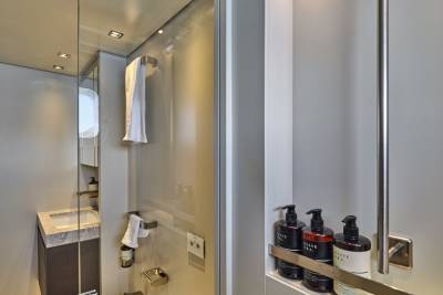 In the foreground, three dark bottles of toiletries sit on a shelf, while the background reveals a compact bathroom with a sink and a towel hanging on a rack.