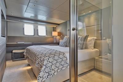 A luxurious yacht bedroom with a patterned bedspread in the foreground and a modern, well-lit interior with windows in the background.