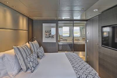 A modern bedroom with a plush bed in the foreground and a glass-enclosed bathroom with a view of the sea in the background.
