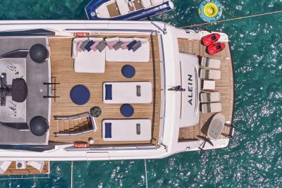 A luxurious yacht with comfortable seating and sun loungers is anchored in clear turquoise water, with a small dinghy and inflatable tubes nearby.