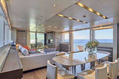 A modern dining table with chairs in the foreground is set against a spacious living area and a backdrop of the ocean visible through large windows.