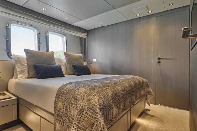 A luxurious yacht bedroom with a neatly made bed in the foreground and a wooden-paneled wall with a door in the background.