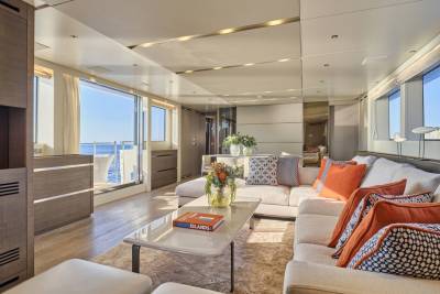 A spacious, modern yacht living area with a large sectional sofa and coffee table in the foreground, and expansive windows overlooking the ocean in the background.