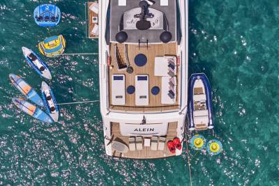 A luxurious yacht is anchored in clear turquoise water, surrounded by inflatable toys and paddleboards.