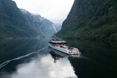 A luxurious yacht cruises through a serene, reflective fjord, flanked by towering, verdant mountains.