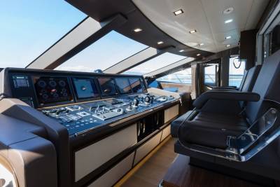 A modern yacht's helm station with multiple screens and controls in the foreground is set against a backdrop of a bright blue sky and distant ocean.