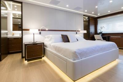 A luxurious bedroom with a large white bed in the foreground and a modern bathroom and desk area in the background.