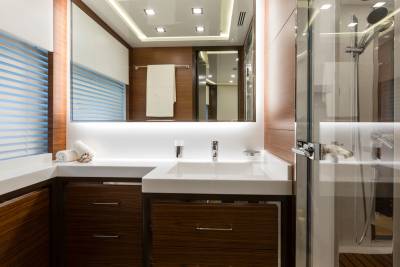 A modern bathroom with a white sink and wooden cabinets in the foreground, and a glass-enclosed shower with a wooden floor in the background.