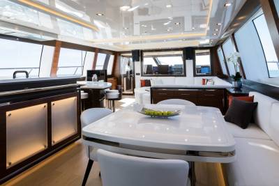 A modern yacht interior features a white dining table with chairs in the foreground and large windows offering ocean views in the background.