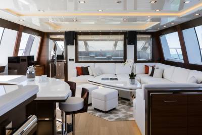 A modern yacht interior features a white bar with stools in the foreground and a spacious white sectional sofa with large windows overlooking the ocean in the background.