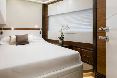 A neatly made bed with pillows in the foreground is set against a backdrop of blinds and cabinetry in a modern cabin.