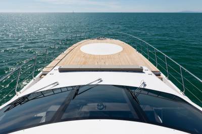 A yacht's bow cuts through the calm, sun-dappled ocean, with a distant hazy coastline on the horizon.