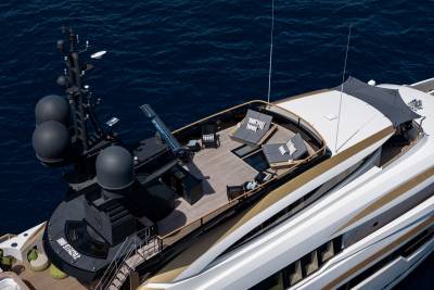 A luxurious yacht with a spacious deck furnished with lounge chairs and tables sits on the deep blue ocean.