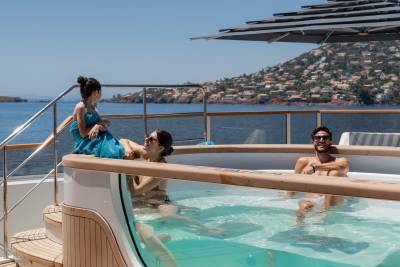 Three people relax in a hot tub on a yacht with a hillside town in the background.