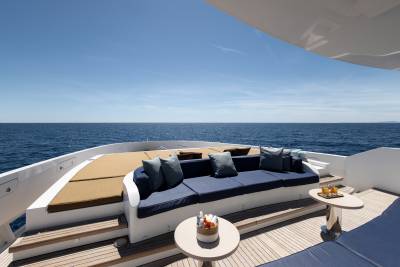 A luxurious yacht deck with a plush blue sofa and sun loungers in the foreground faces a vast, calm blue ocean under a clear sky.