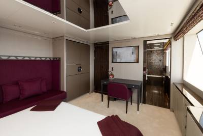 A luxurious bedroom with a plush purple sofa in the foreground and a modern ensuite bathroom visible in the background.