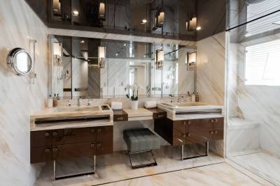 A luxurious bathroom with marble countertops and dark wood vanities in the foreground, and a mirrored wall reflecting the room and a window with blinds in the background.