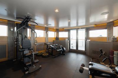 A well-equipped gym with a multi-station weight machine in the foreground and large windows overlooking the ocean in the background.