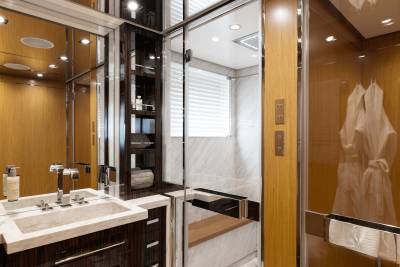 A luxurious bathroom with a marble sink in the foreground and a glass-enclosed shower with white robes hanging in the background.