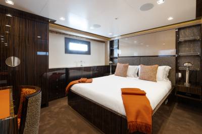 A luxurious bedroom with a large bed in the foreground and dark wood cabinetry and a small window in the background.