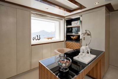 A modern office space with a desk in the foreground and a window overlooking a calm sea and distant hills in the background.