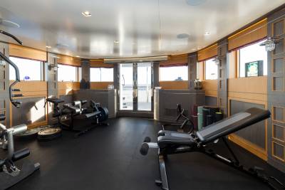 A well-equipped gym with a weight bench in the foreground and large windows overlooking the ocean in the background.