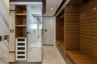 A modern walk-in closet with mirrored doors and wooden shelving in the foreground is contrasted by a white door and more wooden accents in the background.