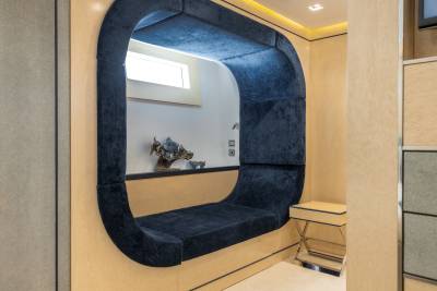 A dark blue, curved alcove with a built-in bench is set into a light-colored wall, with a small table and a window visible in the background.