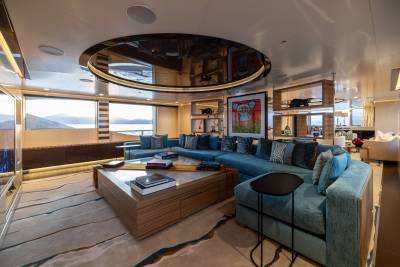 A spacious, modern living area with a large sectional sofa and coffee table in the foreground, and large windows offering a view of the sea and distant hills in the background.