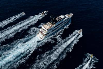 A large white yacht cruises through the deep blue ocean, trailed by several smaller boats creating white wakes.