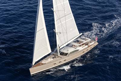 A sleek sailboat with full sails glides across the deep blue ocean, leaving a white wake behind it.