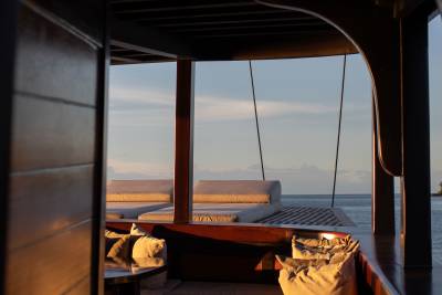 Sunlight warms the plush seating in the foreground, while the tranquil ocean stretches to the horizon under a soft sky in the background.