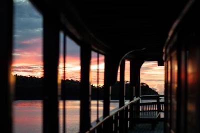 Silhouetted railings frame a tranquil ocean and a vibrant sunset over a distant, tree-lined shore.