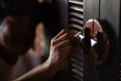 A person's hand polishes a wooden star-shaped knob on a dark wooden door with a textured background.