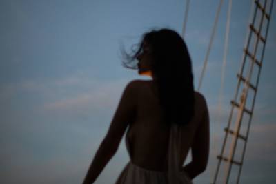 A woman with dark hair stands on a boat against a twilight sky, with a ladder visible to her right.