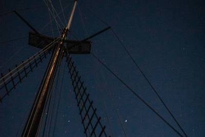 A tall mast with rigging extends upwards into a dark, starry night sky.