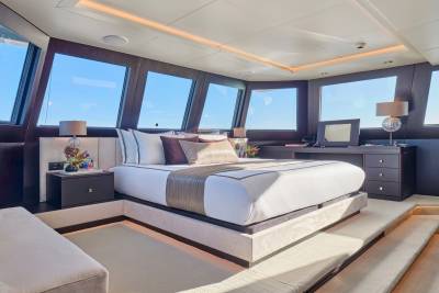 A luxurious bedroom with a large bed in the foreground and large windows offering a view of the ocean in the background.