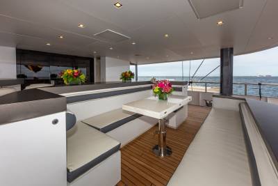 A modern yacht deck with white cushioned seating and a table in the foreground, and the ocean and sky in the background.