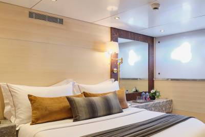 A neatly made bed with plush pillows occupies the foreground, while a mirrored wall reflecting soft lighting and a hint of the room's interior forms the background.
